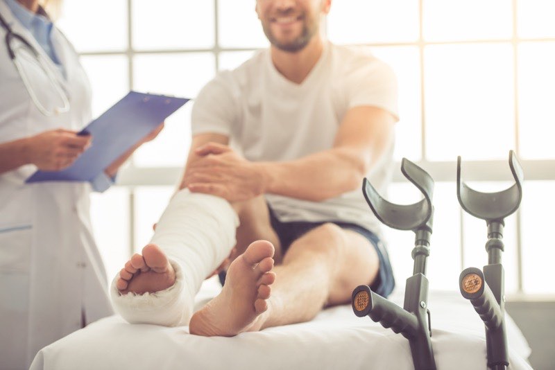 An injured employee with a leg cast and crutches meeting with a clinician